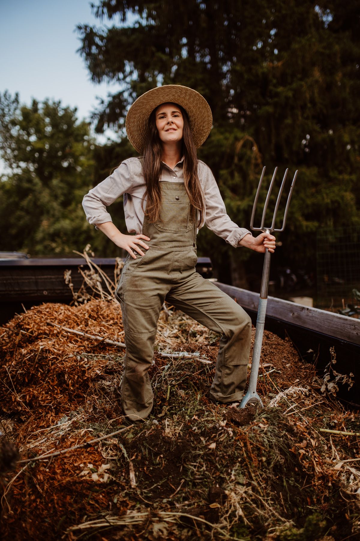 A gardener with a fork beside a compost pile